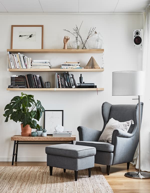 Three wall shelves and a bench are placed near a great armchair and footstool.