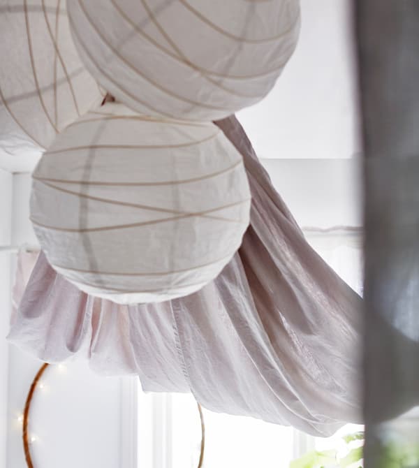 Three white paper lanterns hang from the ceiling in a bright, white dorm room.