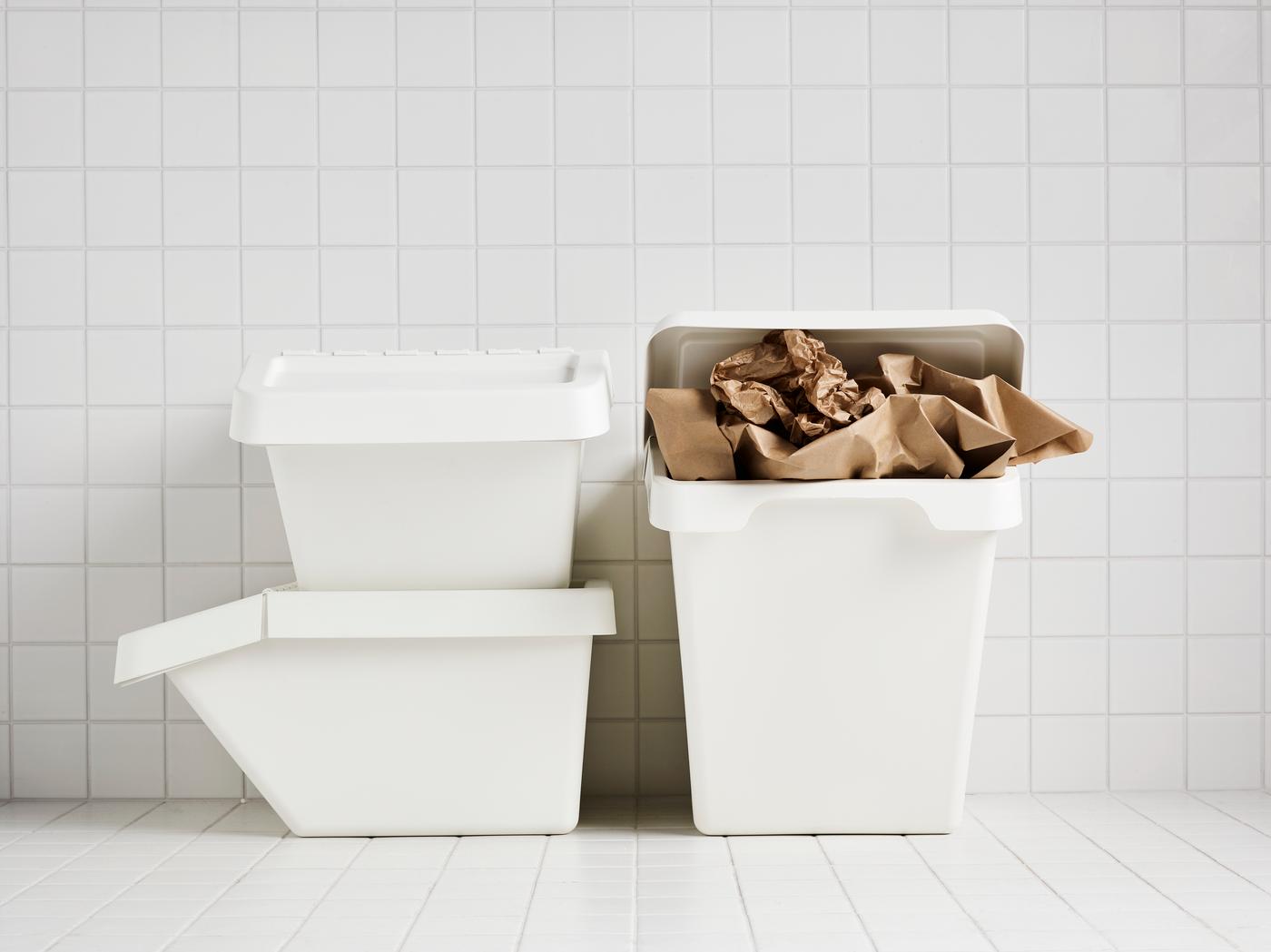 Three white SORTERA bins in a white tiled room where one is stuffed with brown paper.