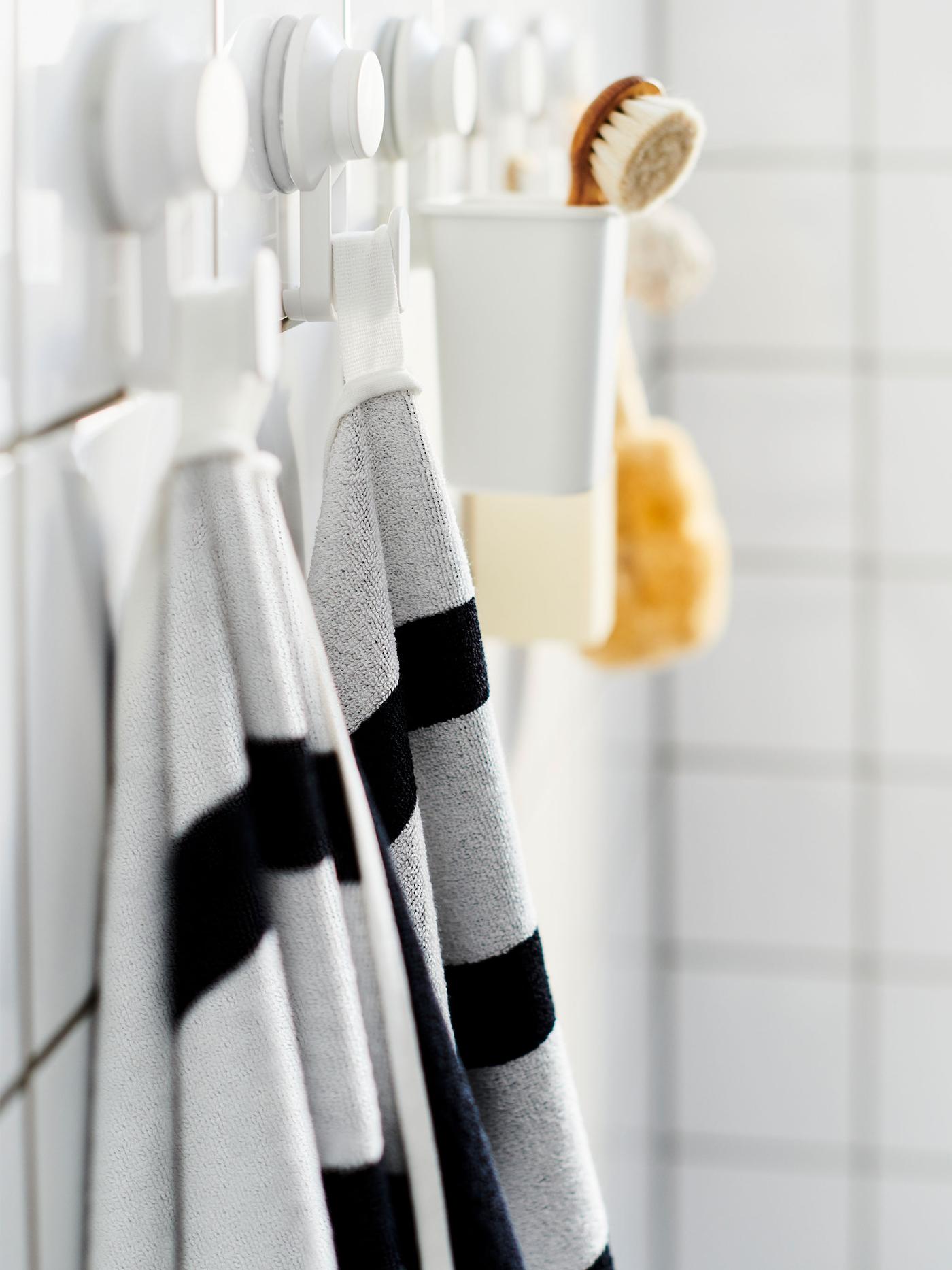 Tiled bathroom wall with a row of TISKEN suction-cup hooks, holding towels, a scrubber, and similar accessories.