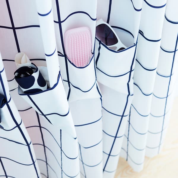 Tissu bleu et blanc IKEA ROSALILL avec poches cousues dessus pour des lunettes, une brosse et d’autres petits accessoires.