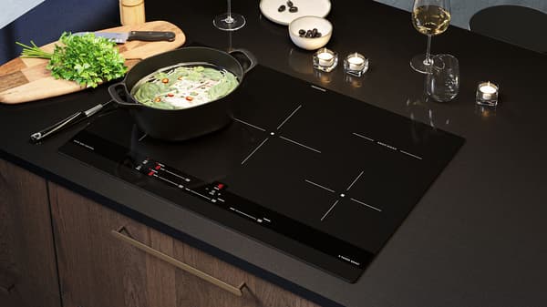 Top-down shot of a cooktop appliance built into a black countertop iwth a black dish cooking on top.