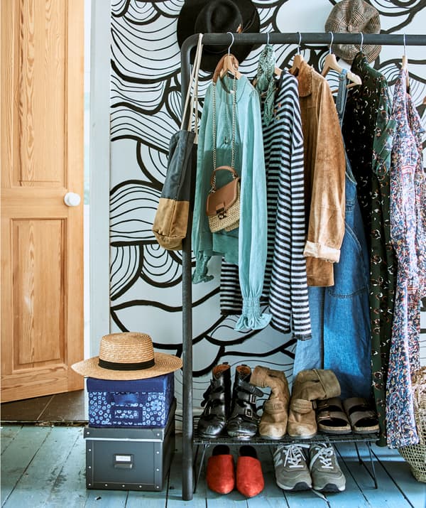 Tops, dresses and jackets hanging on a clothes rail with storage boxes piled beside it and shoes on a rack below it.
