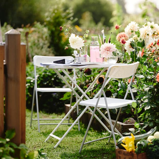 TORPARÖ outdoor table and folding chairs in the garden with dining ware and other items on top of the table.