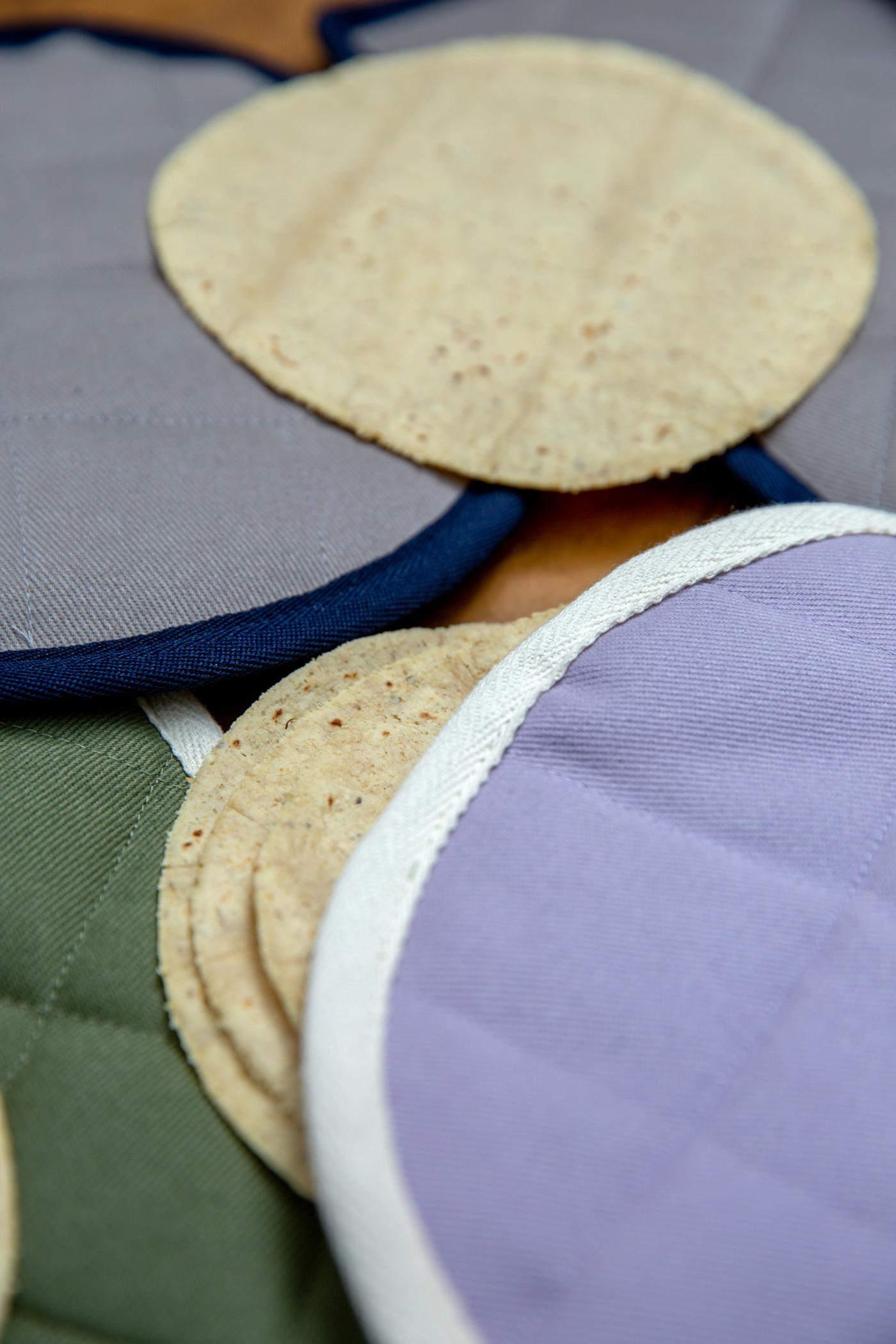 Tortilleros, de varios colores extendidos sobre superficie junto con tortillas.