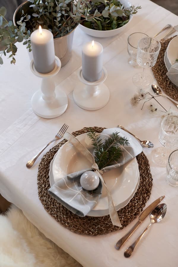 Tovaglioli decorati con un rametto di abete, posti su un piatto, con accanto posate e candele.