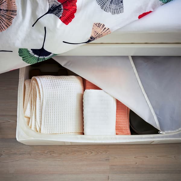 Towels stored in a zip-cover box under the side of a bed with floral bedding.