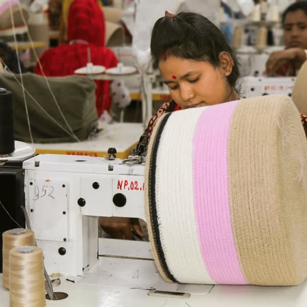 Trabajadora confeccionando un rollo grande de tela con rayas en beige y rosa con una máquina de coser.