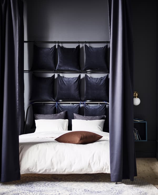 Transformez un lit en nid douillet à l’aide de quelques articles IKEA. Délimitez d’abord le pourtour du lit en utilisant des tringles et des crochets fixés au plafond. Puis, accrochez-y des rideaux, comme les SANELA en velours de coton bleu foncé, qui bloqueront la lumière et absorberont le bruit.