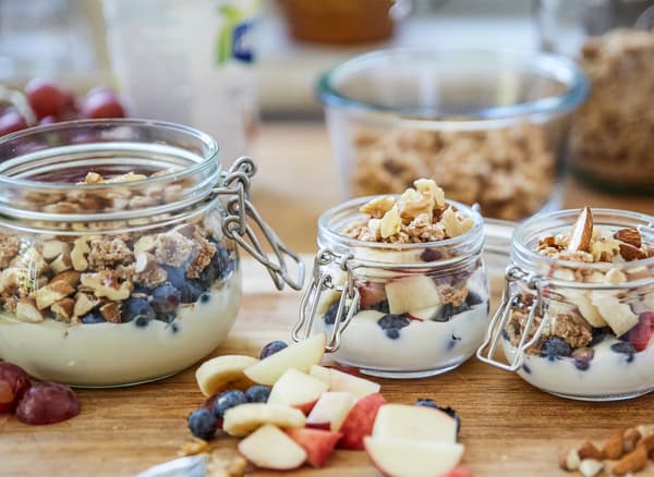 Tre contenitori in vetro contenenti yogurt, granola, frutta fresca e noci su un piano di lavoro in legno - IKEA