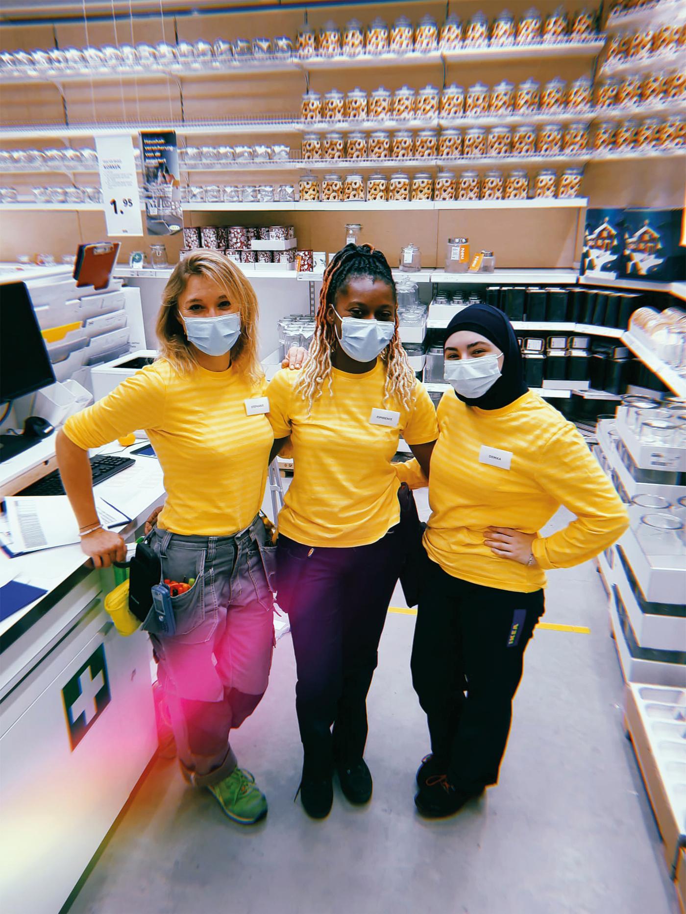 Trois collaboratrices IKEA debout côte à côte, portant des hauts jaunes et des masques.