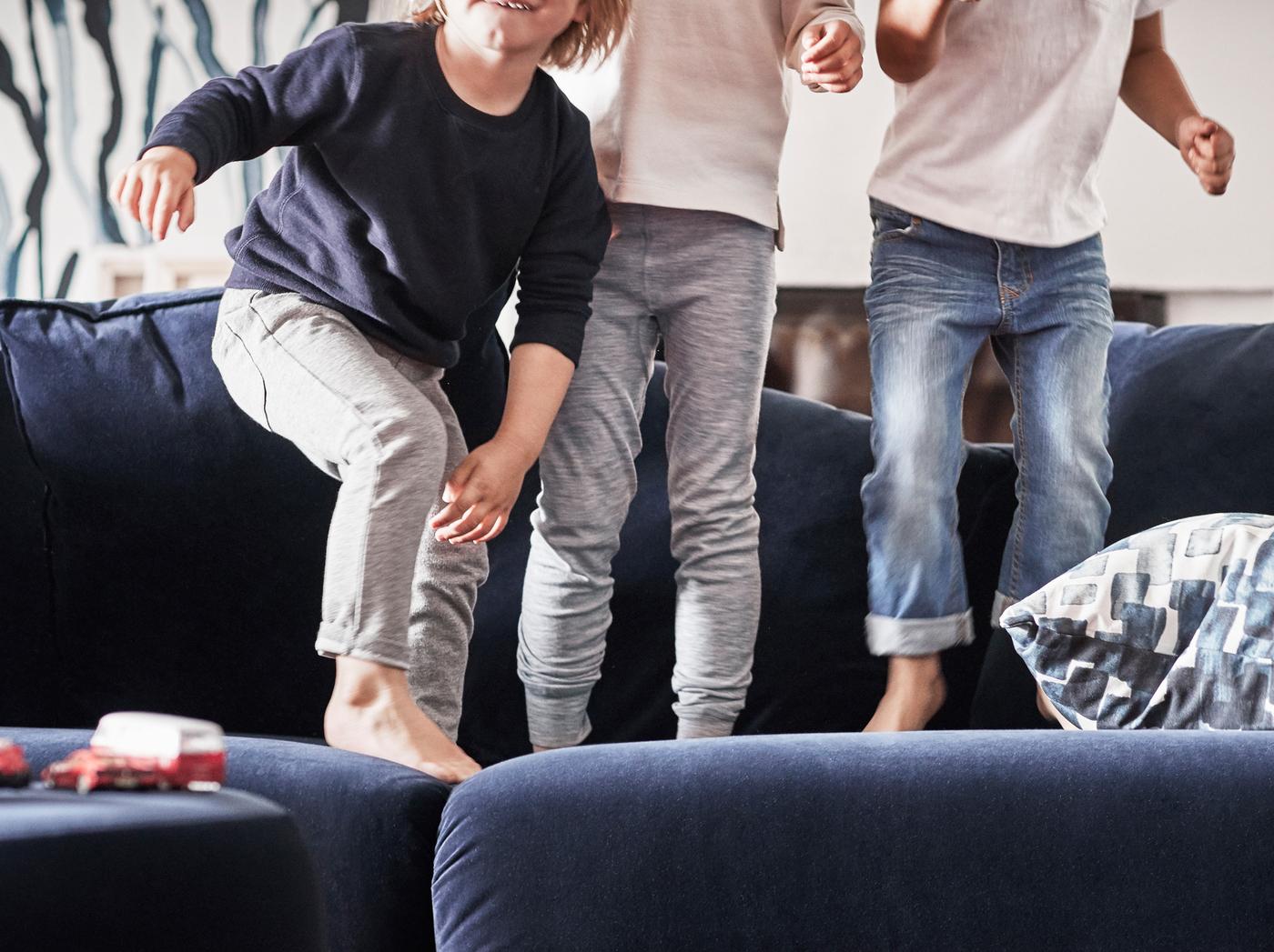 Trois enfants, pieds nus, en train de sauter sur un canapé bleu foncé.