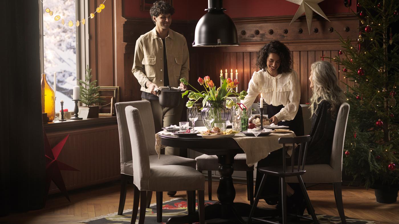 Trois personnes se réunissent autour d'une table ronde INGATORP décorée de fleurs fraîches afin de partager un repas des Fêtes.