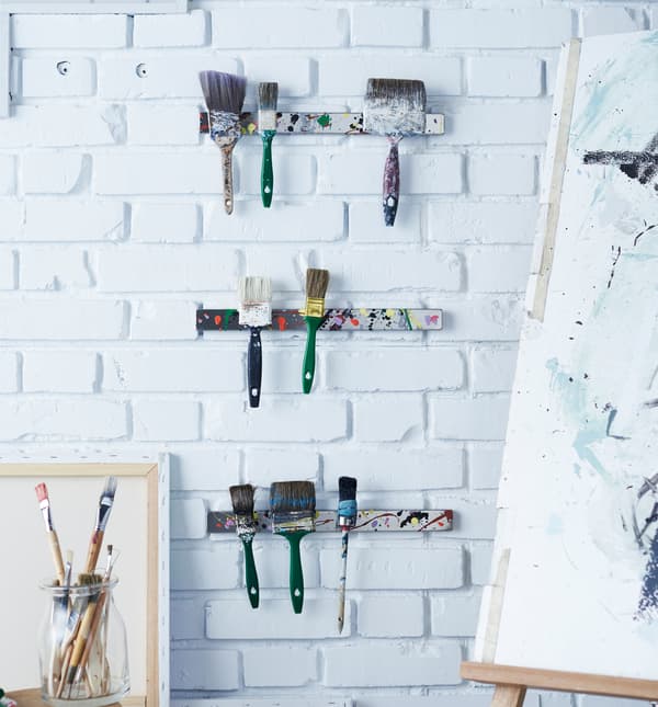 Trois rails à couteaux magnétiques servant de rangement à des pinceaux au mur d’un studio d’art.