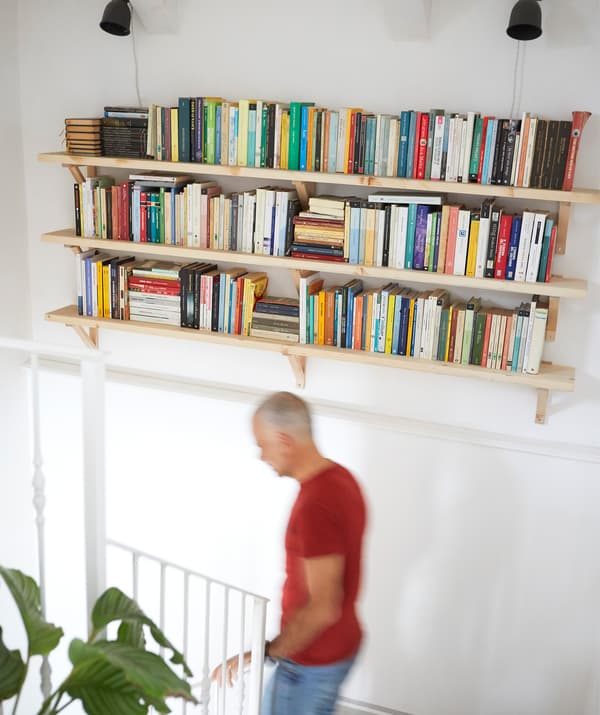 Trois tablettes remplies de livres accrochées à un mur blanc au-dessus d'un escalier.