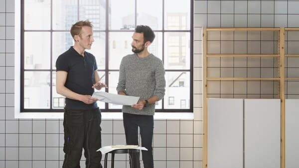 Två män med en ritning i handen diskuterar.