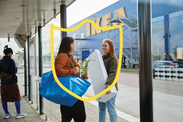 Twee mensen bij een bushalte houden spullen vast die ze gekocht hebben in het IKEA woonwarenhuis aan de overkant.