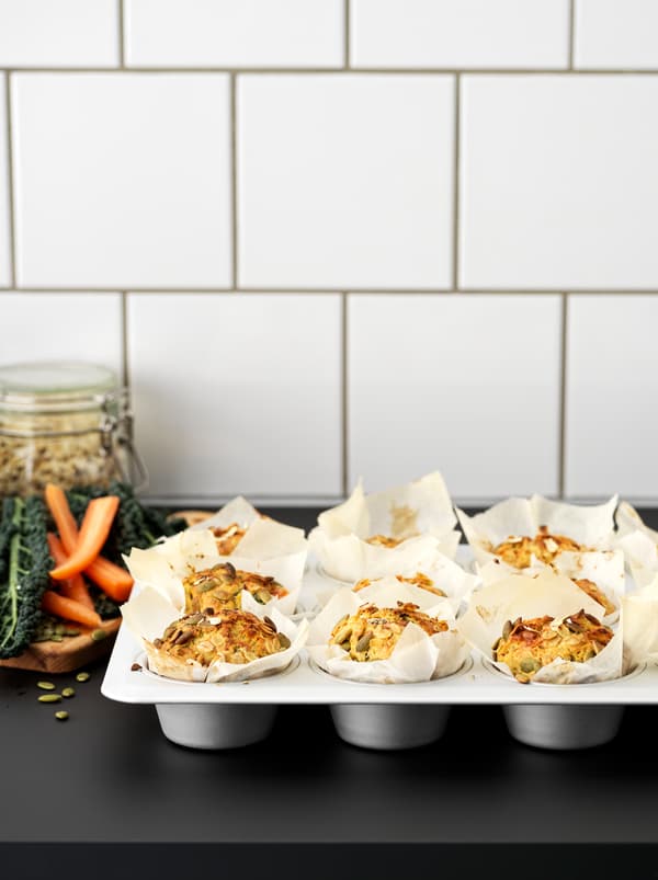 Twelve muffins made with pumpkin seeds and carrots in a VARDAGEN metal muffin tin on a black kitchen worktop.