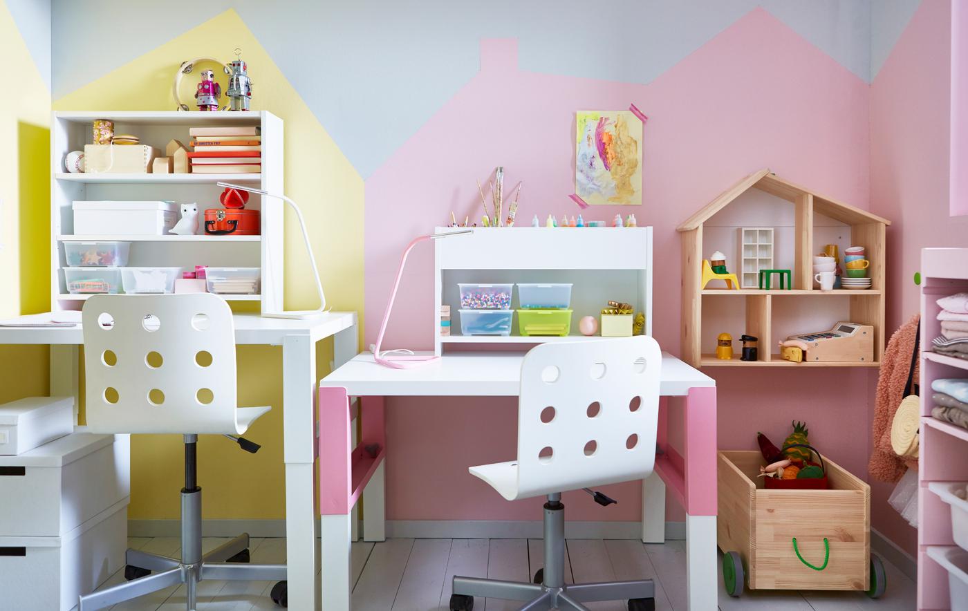 Two adjustable desks and chairs side-by-side in a shared kids’ room, with some storage units and a dolls house.