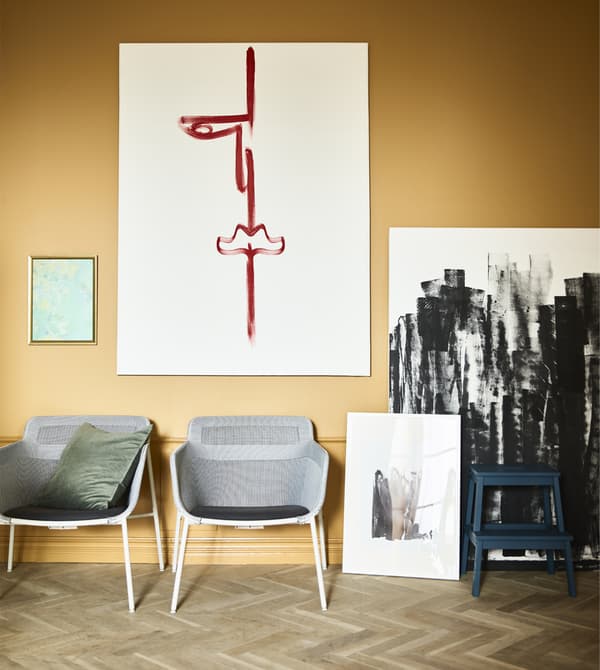 Two armchairs and canvases of art sit against a wall.
