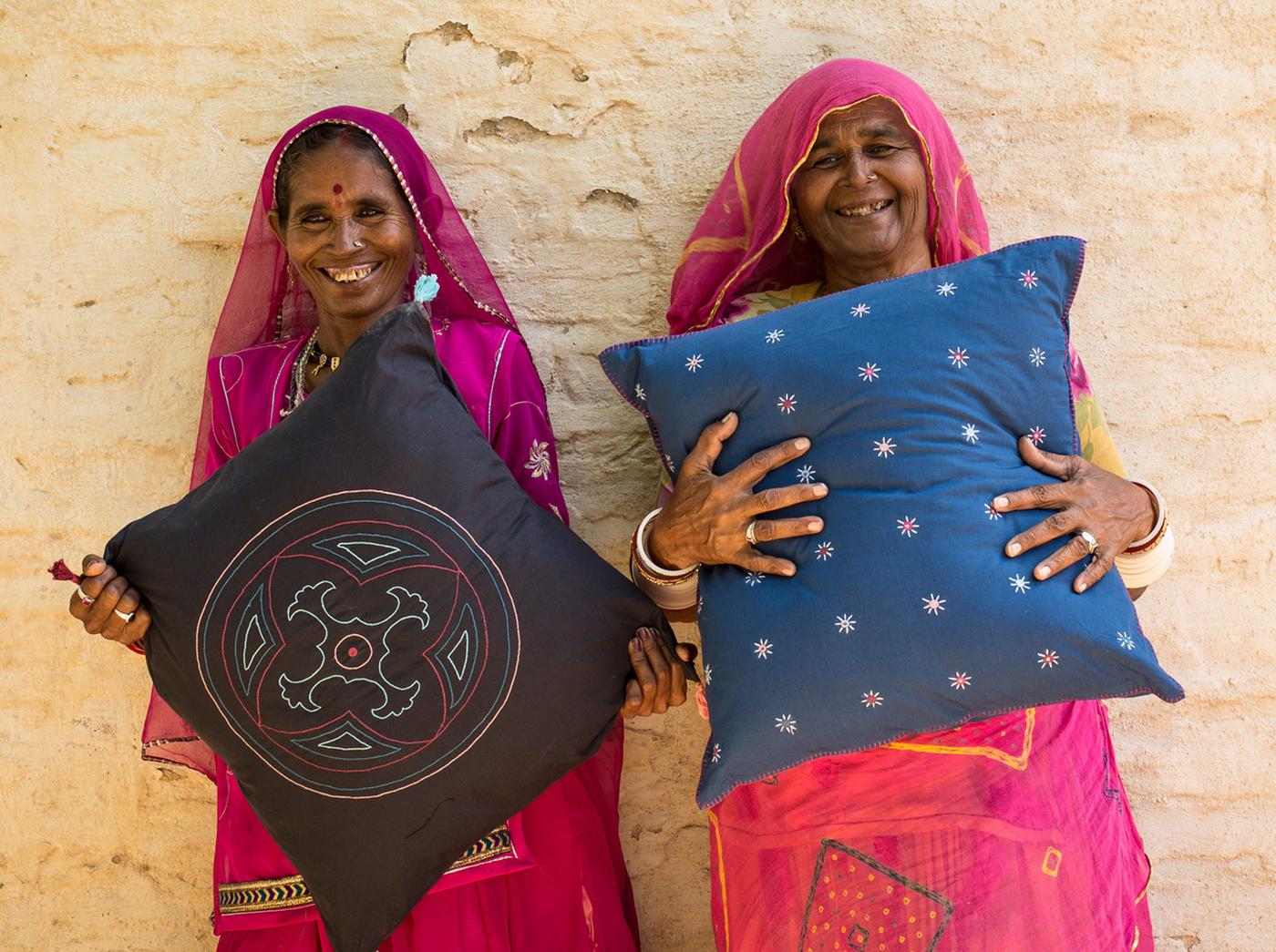 Two artisan women working with a social entrepreneur in India are holding up the handcrafted pillows they made for IKEA.