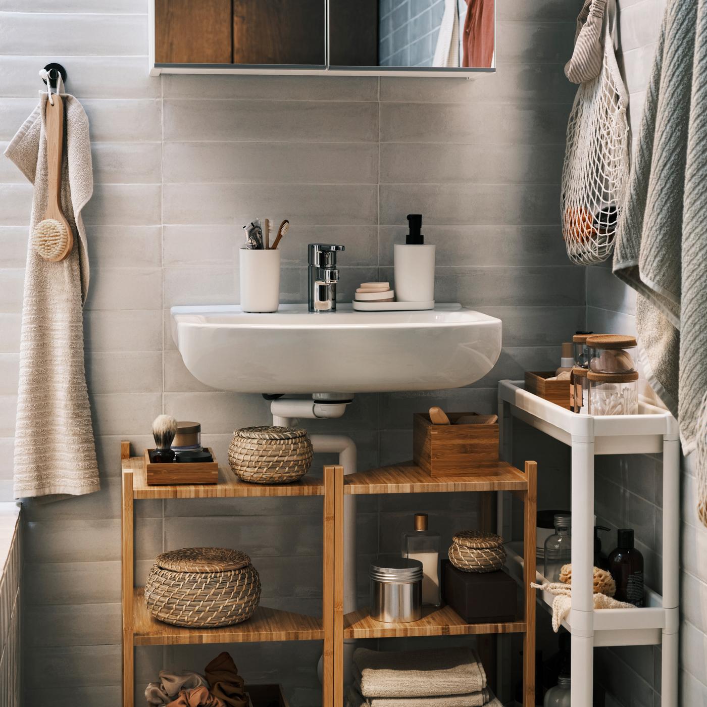 Two bamboo wash-basin/corner shelves under a wash-basin with a white mirror cabinet over it, plus a trolley and a hand towel.