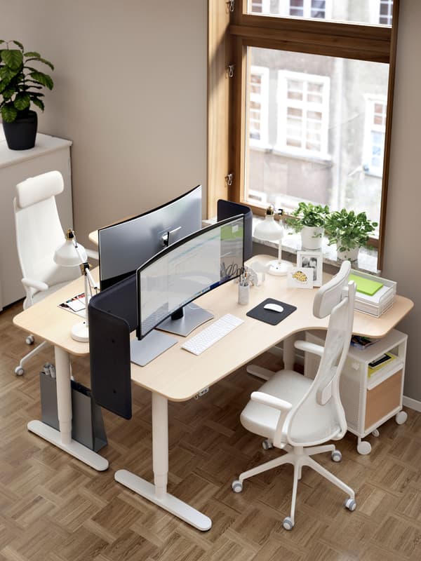 Two BEKANT corner desks facing each other beside a large window. Each desk has a JÄRVFJÄLLET chair and a BEKANT storage unit.