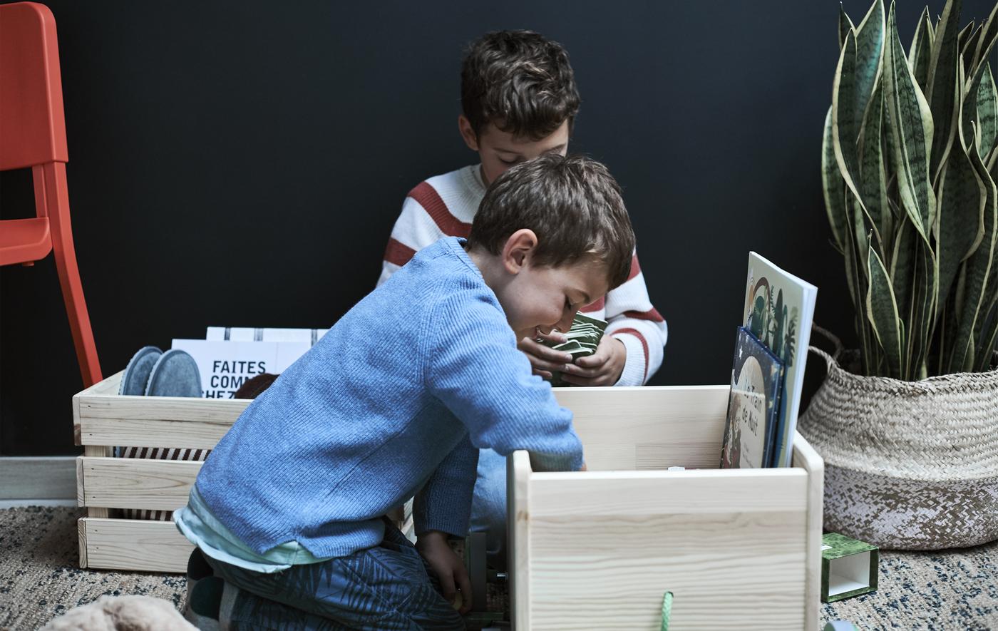 Two boys looking inside a wooden box filled with objects.