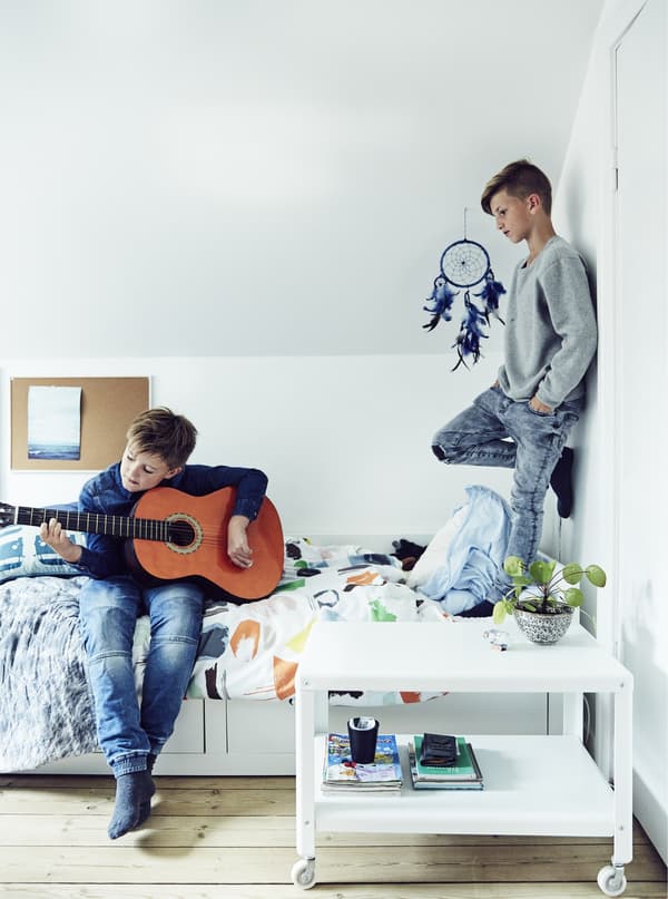 Two boys playing in a child’s bedroom, one standing on the bed, the other playing a guitar.
