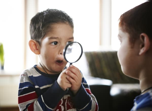 Two boys sitting in front of each other, one of them making funny faces through a magnifying glass.