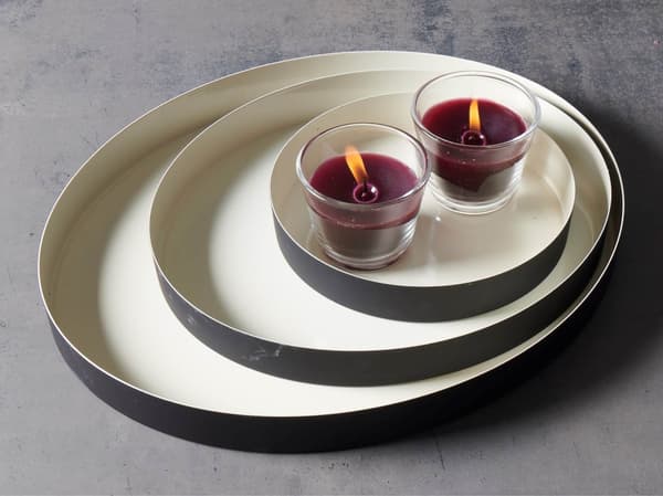 Two burning purple candles in glass holders stand together on a set of stackable trays reminiscent of a minimalist IKEA display.