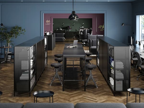 Two centrally placed black BEKANT shelving units with BEKANT desk and TROLLBERGET active sit/stand supports between them.