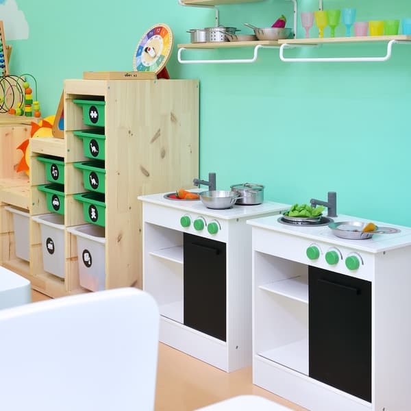 Two children cooking area placed against a turqoise wall. Storage cabinets are placed beside.