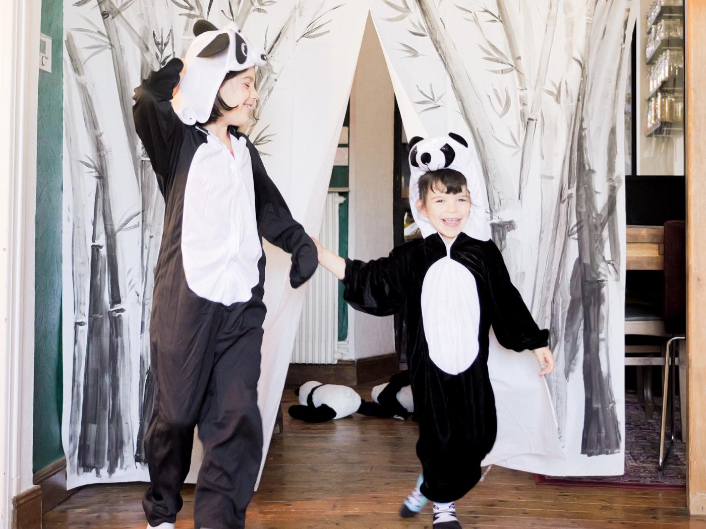 Two children in panda bear costumes take a bow in front of a stage curtain made from a decorated BJÄRSEN shower curtain.