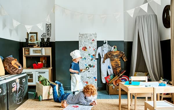 Two children playing in a room with small table and chairs, blackboard, miniature kitchen and bunting.