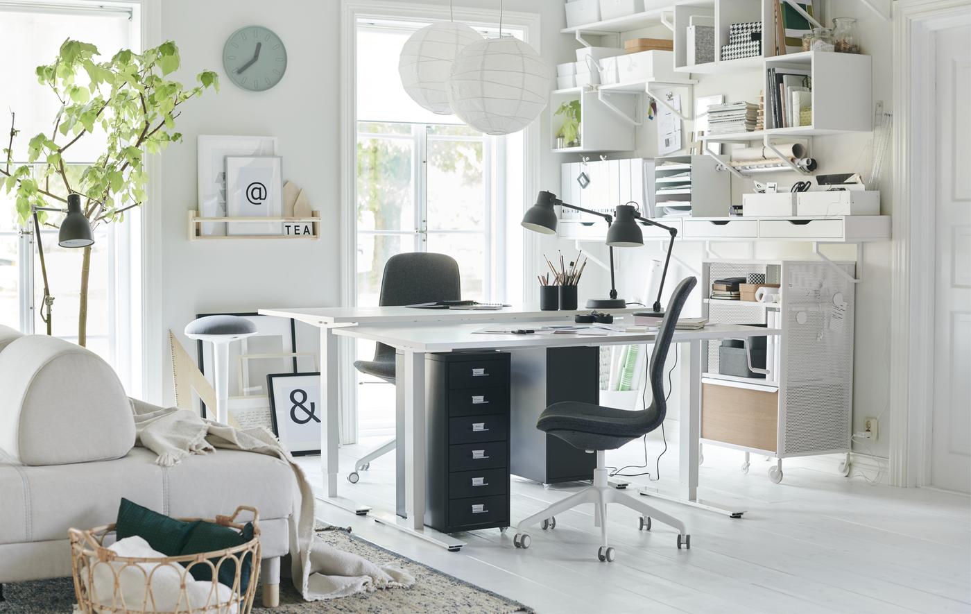 Two desks and desk chairs in the corner of a white living room with wall storage.