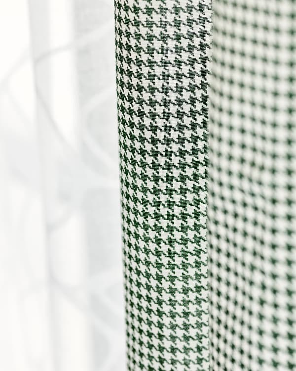 Two fabric curtains hung side by side, one in sheer white cotton, one in green and white check.