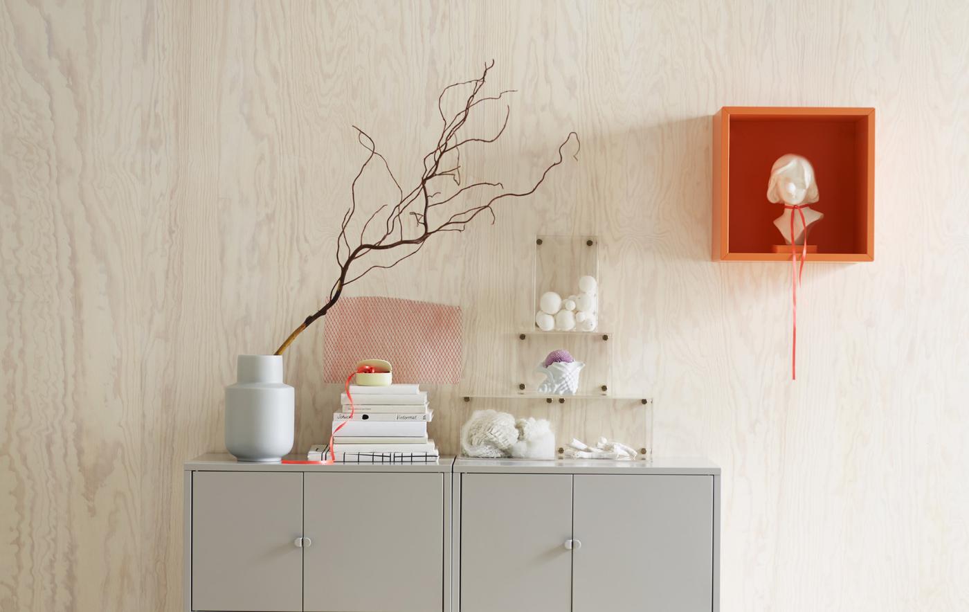 Two grey cabinets against a pine wall in fresh natural lighting, including an orange EKET wall mounted cabinet with a statue.