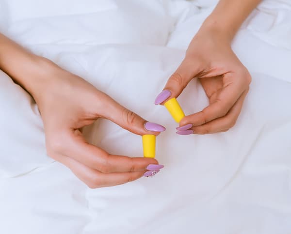 Two hands holding two yellow ear plugs.