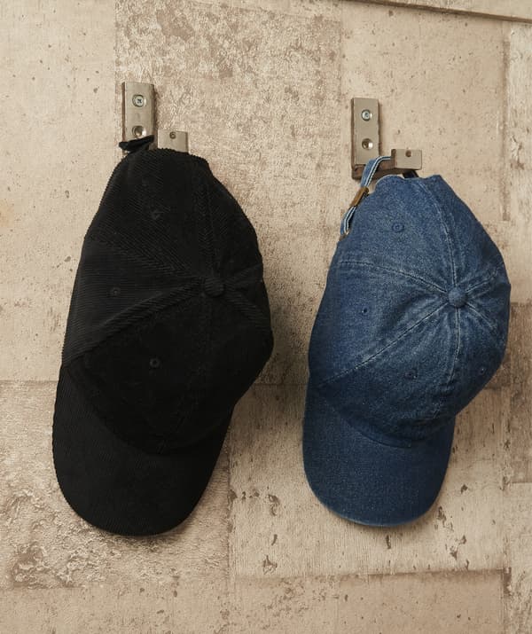 Two hats hanging on silver hooks on a brick wall.
