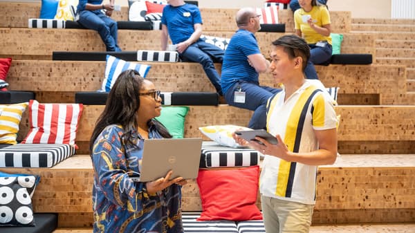 Two IKEA co-workers dressed in casual clothes enjoying a chat and coffee while sitting on wooden stairs.