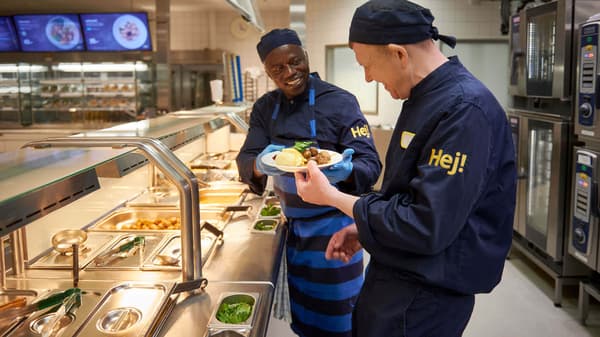 Two IKEA co-workers dressed in dark blue uniforms enjoying a laugh over a snack.