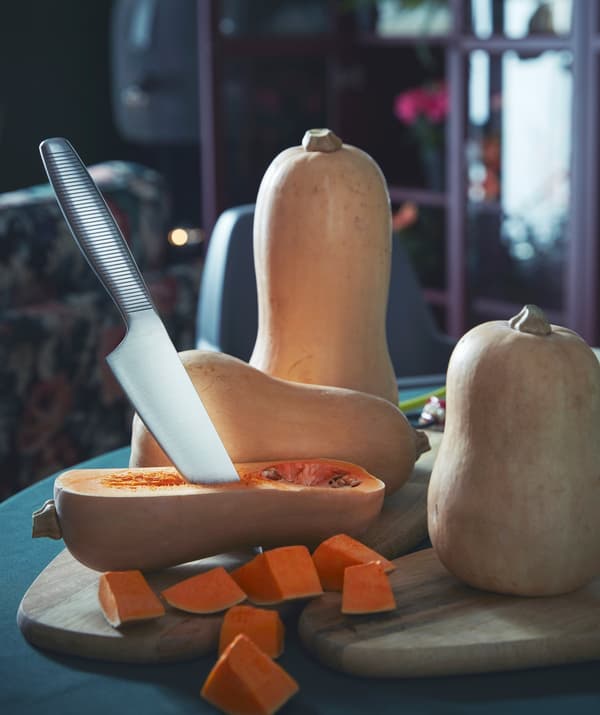 Two IKEA FASCINERA cutting boards placed on a dining table and being used to slice and dice butternut squash.