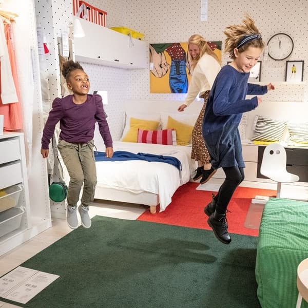 Two kids and a woman is jumping in IKEA showroom.