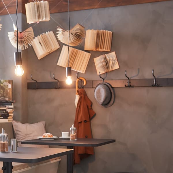 Two light bulbs with a black chord hanging from the ceiling and a wall rack with hooks and a hat and an umbrella on it.