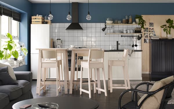 Two NORRÅKER bar tables and five barstools in birch, shown in a blue, white and light wood open kitchen.