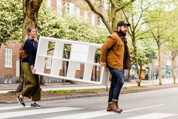 Two people carrying an IKEA Kallax shelving unit across the road to sell it back to IKEA