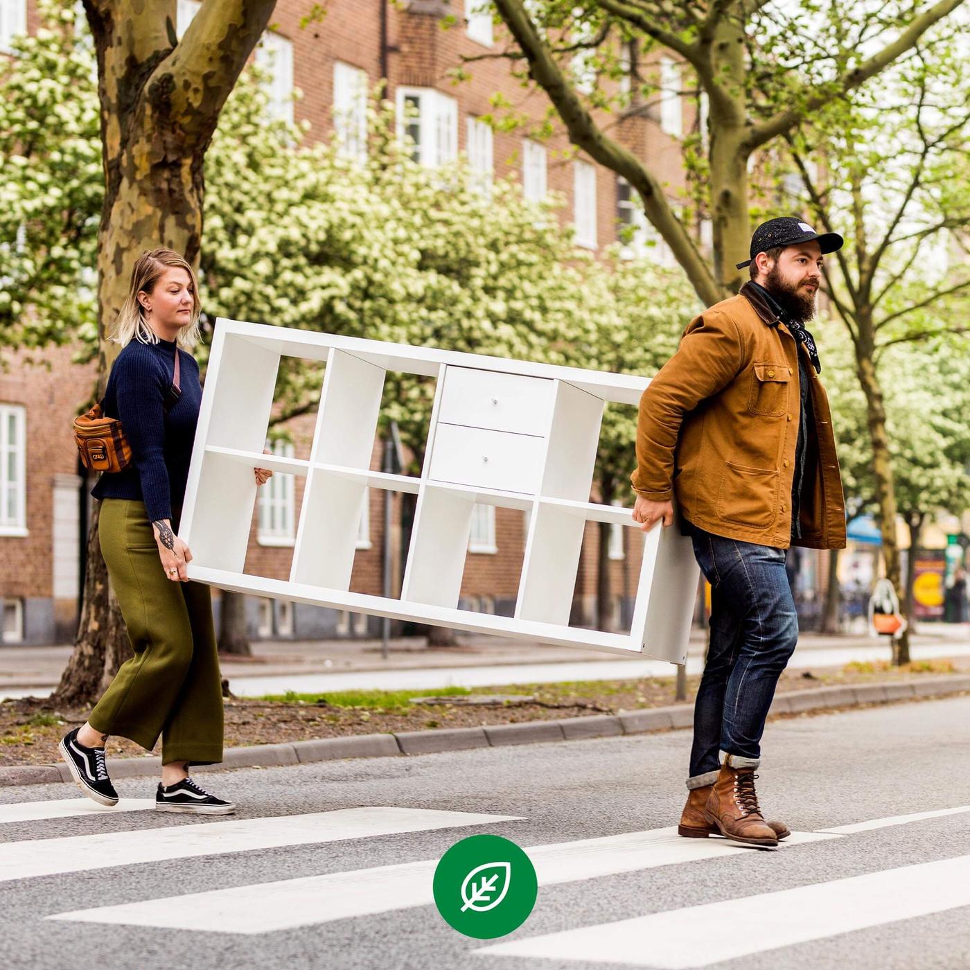 Two people crossing the street carrying a KALLAX shelving unit