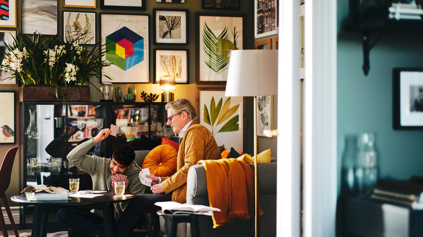 Two people playing cards on a black KRAGSTA coffee table with a gallery wall behind them with assorted framed BILD posters.