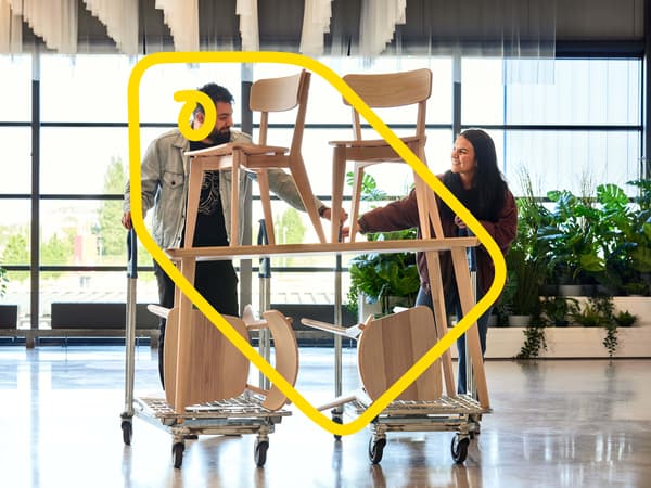 Two people pushing trolleys where a table and four chairs in a wooden finish rest on top.